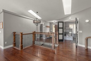 A spacious interior with a wooden staircase, a chandelier, and a view into a bedroom area.