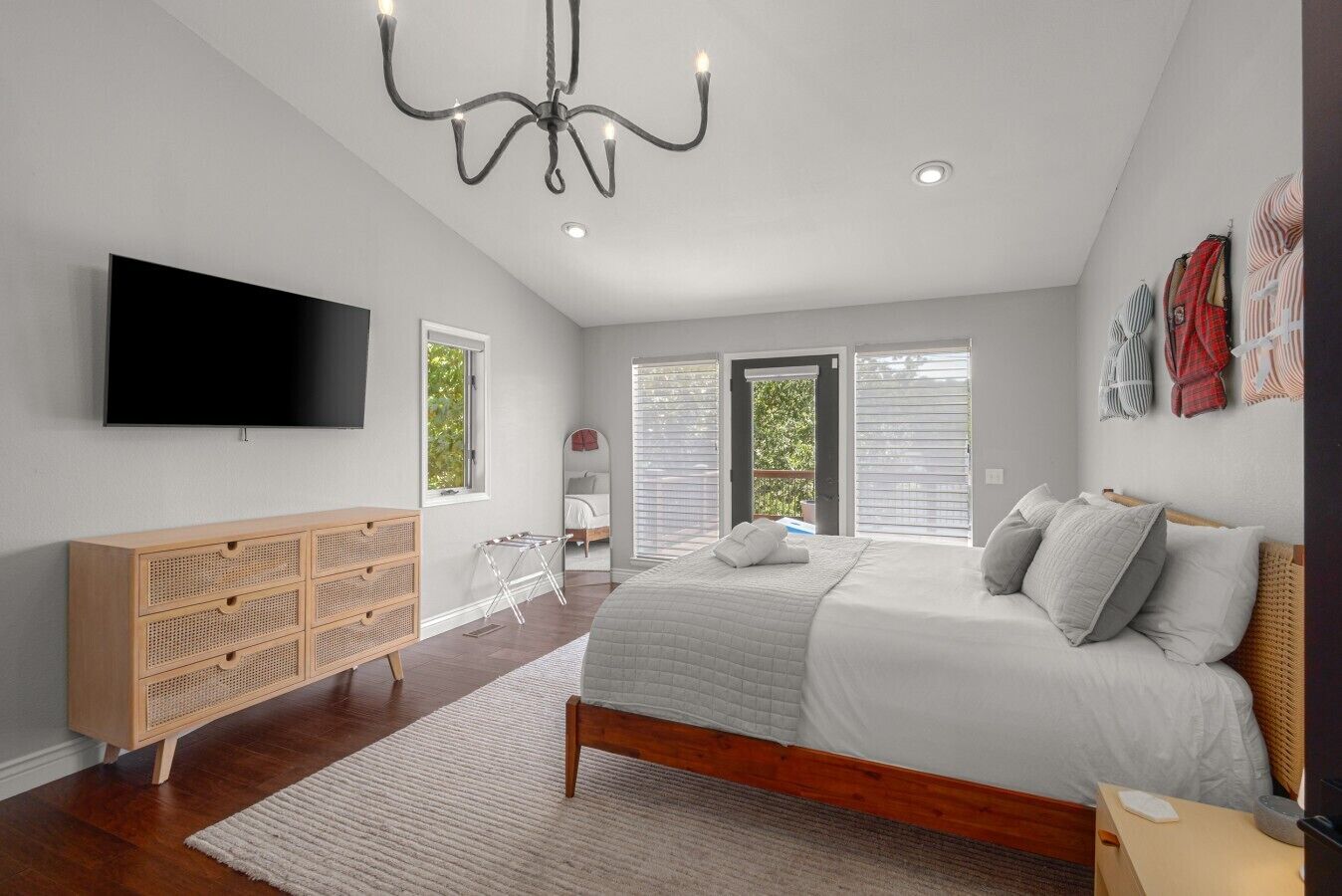 A bedroom with a large bed, a wooden dresser, a flat-screen TV, and a chandelier.