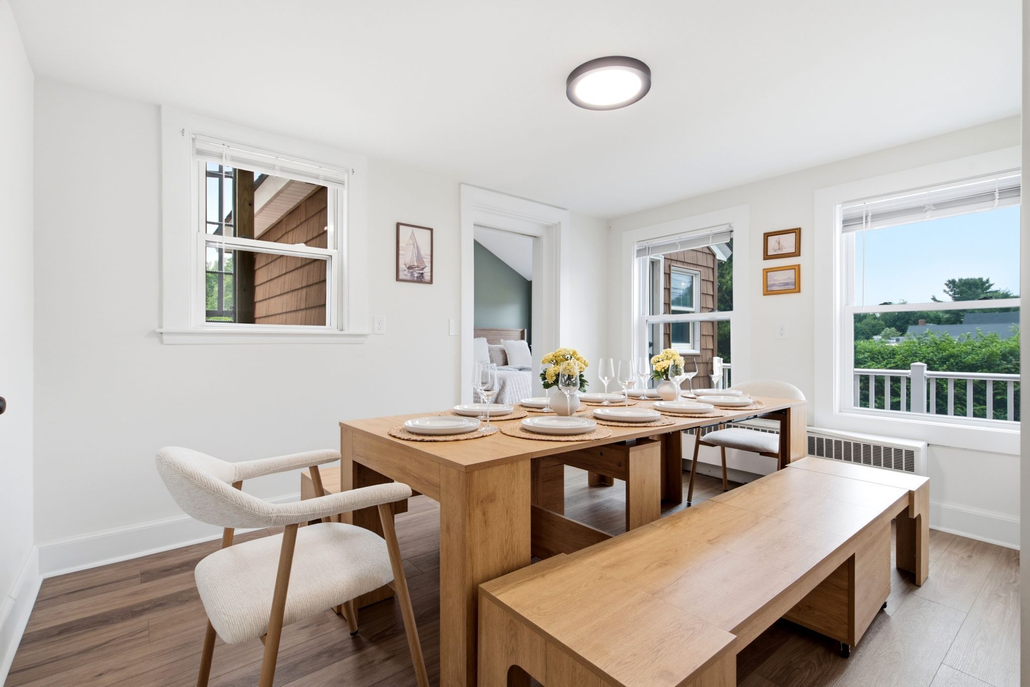 A dining area with a wooden table set for six, white chairs, and a bench.