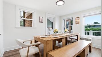 A dining area with a wooden table set for six, white chairs, and a bench.