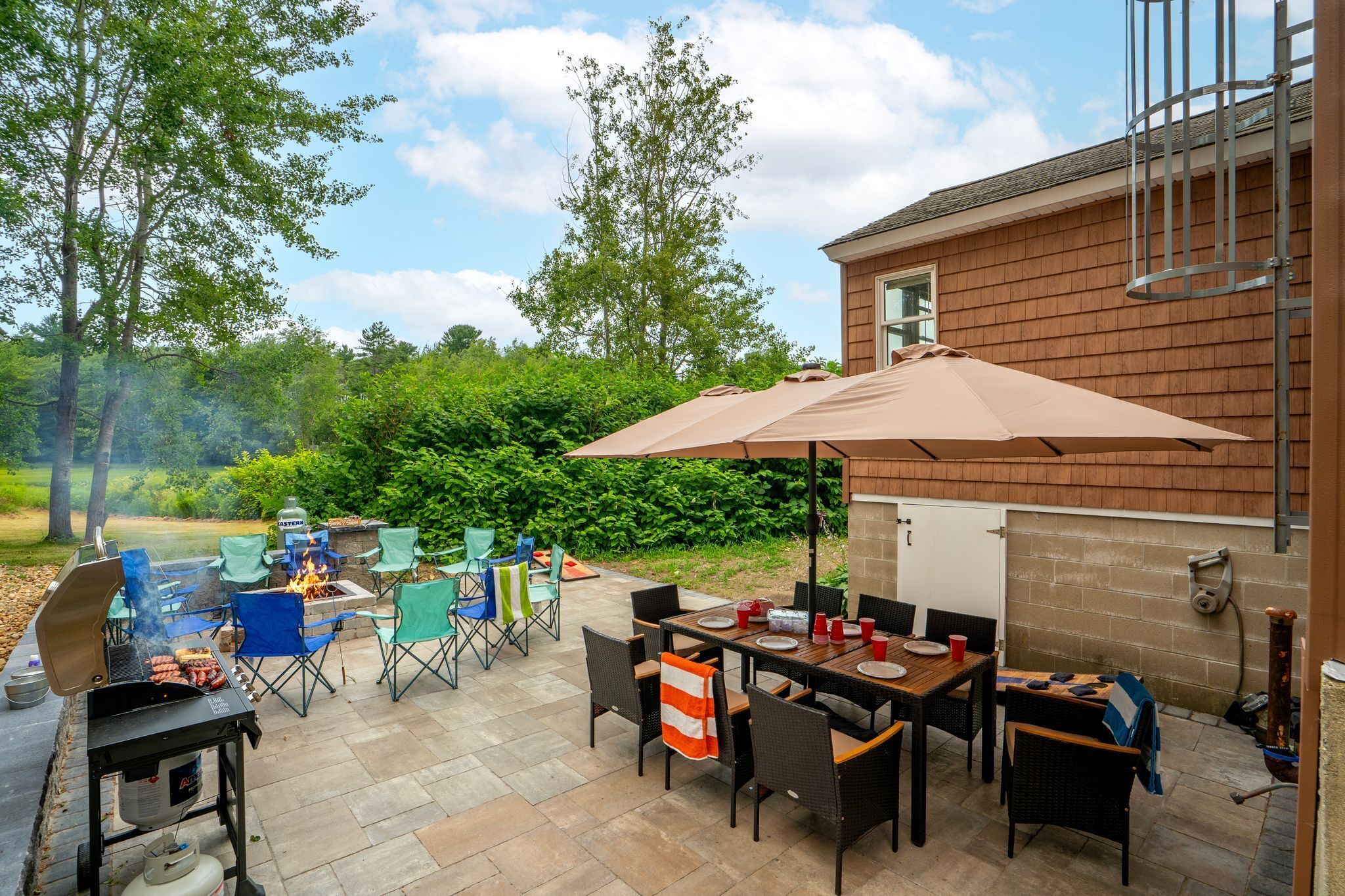 En udendørs patio med grill, spisebord, stole og parasol.