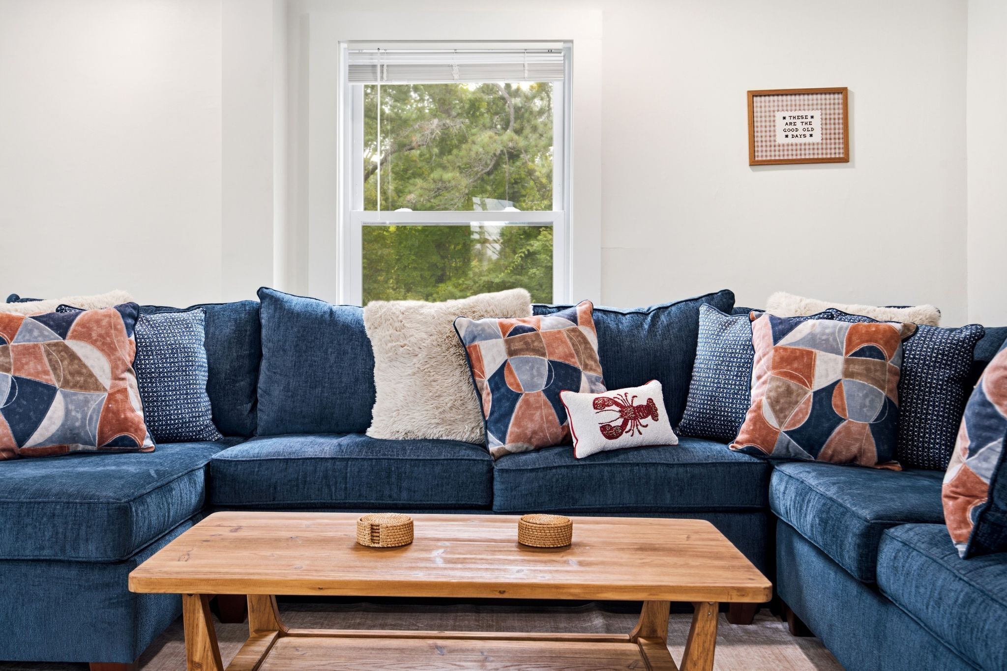 A living room with a blue sectional sofa, a wooden coffee table, and a window with blinds.