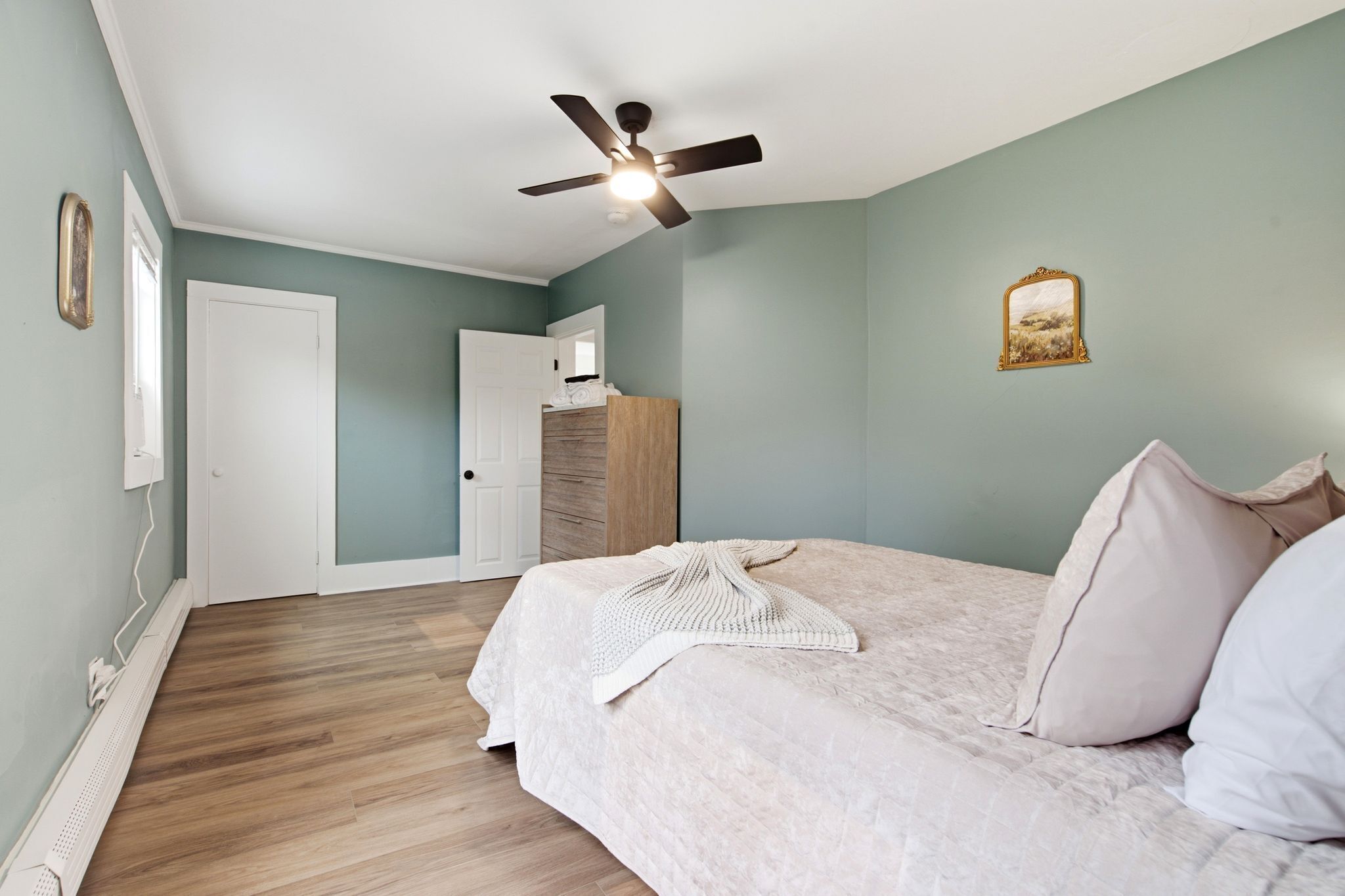 A bedroom with a bed, a ceiling fan, a dresser, and a door.