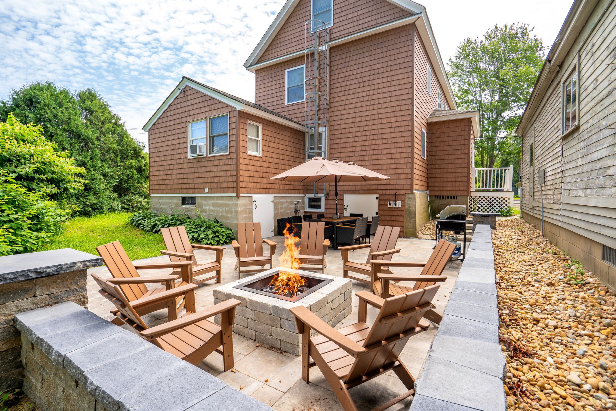 Une terrasse avec un foyer extérieur, du mobilier de jardin et un espace barbecue.