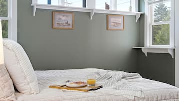 A bedroom with a bed, a bedside table with a glass of orange juice, and two framed pictures on the wall.