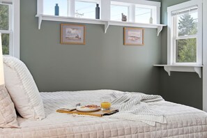 Ein Schlafzimmer mit einem Bett, einem Nachttisch mit Orangensaft und zwei gerahmten Bildern an der Wand.