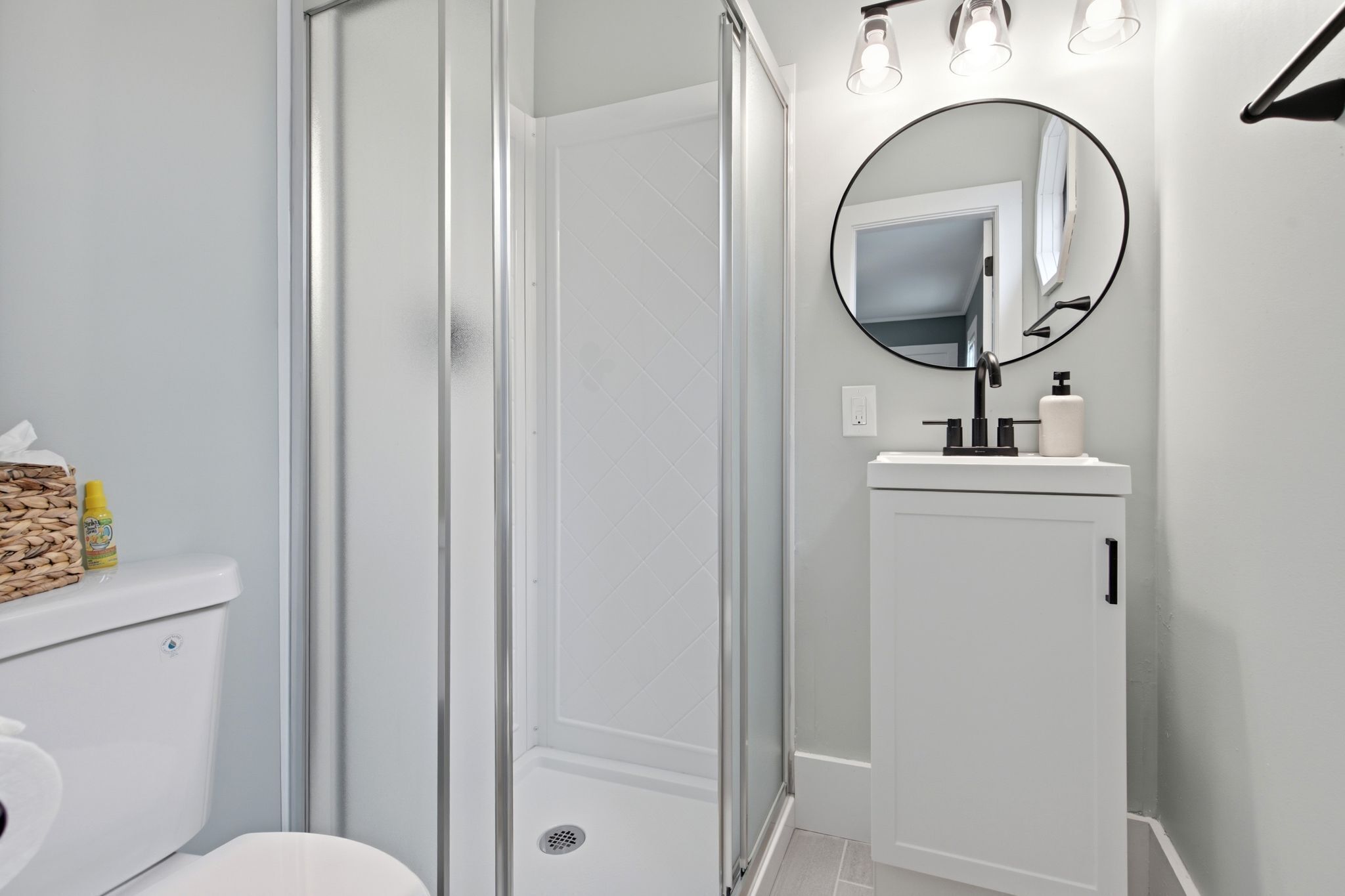 A bathroom with a toilet, a shower enclosure, a sink with a mirror, and a towel dispenser.