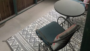 Une véranda abritée avec une table et des chaises, un petit tabouret et une vue sur une zone boisée.