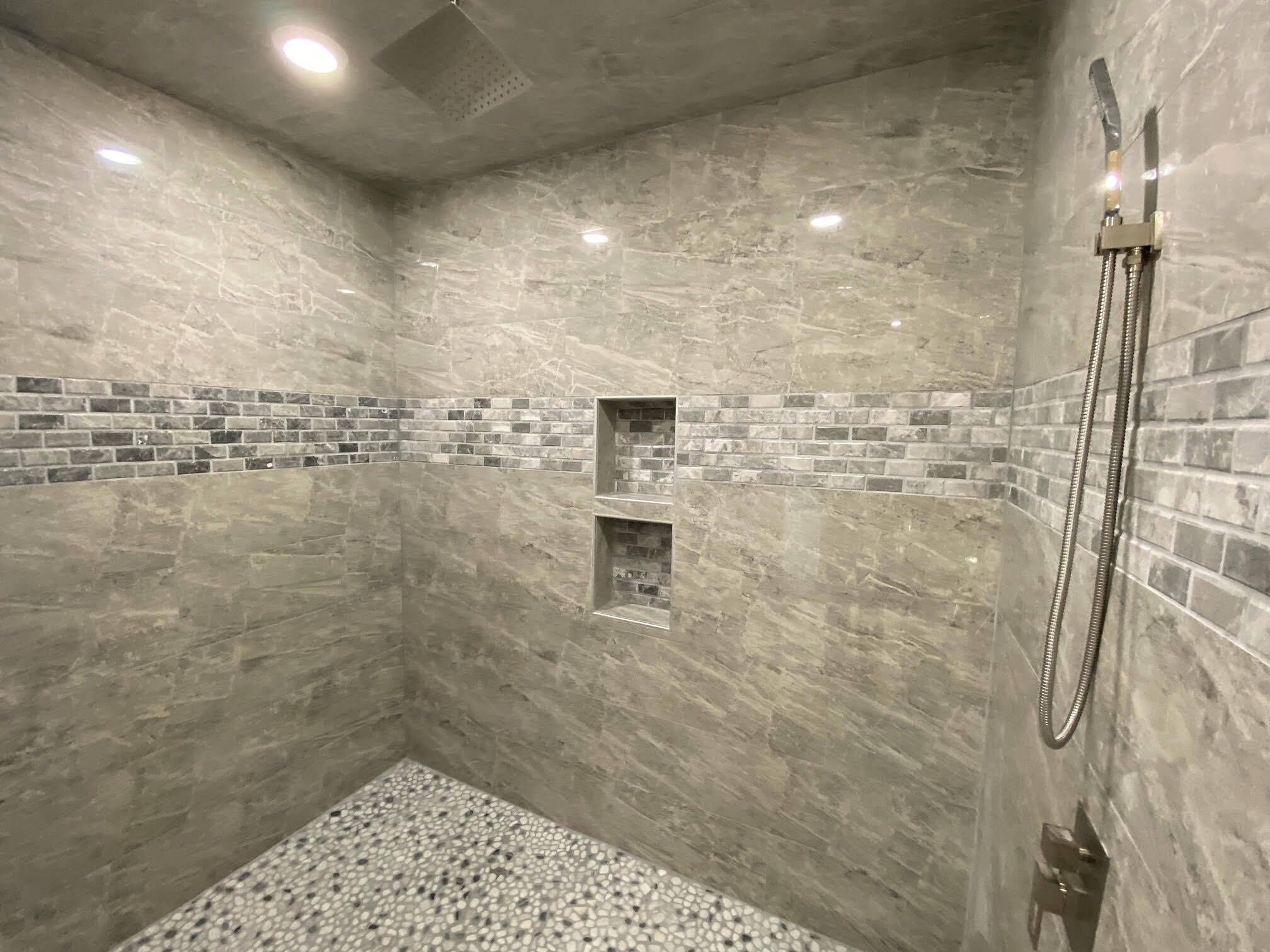 Una ducha con cabezal de ducha manual, piso de azulejos y un pequeño armario de pared.
