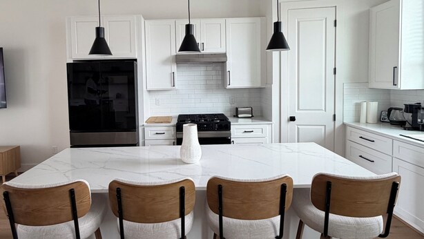 Una cocina moderna con armarios blancos, una isla central con taburetes y luminarias colgantes.