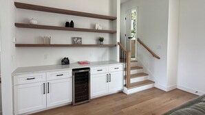 Una sala moderna con cocina integrada, estanterías de madera, una escalera y un horno empotrado.