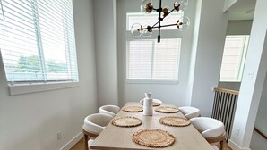 Comedor con mesa de madera, seis sillas, individuales tejidas y una lámpara moderna.