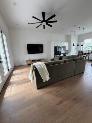 Ein modernes Wohnzimmer mit einer großen Couch, einem Flachbildfernseher und einem Deckenventilator.