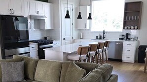 Una cocina moderna con armarios blancos, un refrigerador negro y un comedor con sofá y sillas.