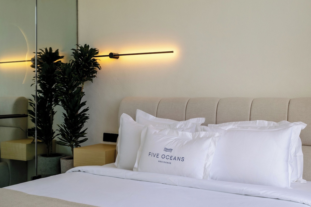 A modern hotel room with a large bed, a bedside table, a mirror, and a wall-mounted light fixture.