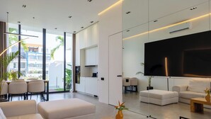 A modern living room with a large flat-screen TV, a sofa, a coffee table, and a dining area with chairs and a table. - Five Ocean Residence (Badung)