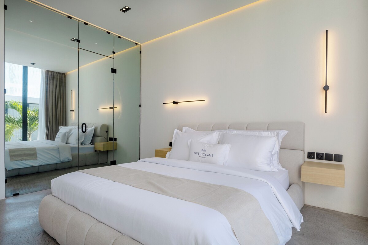 Una habitación de hotel moderna con una cama grande, una mesita de noche, una lámpara de pared y un espejo.