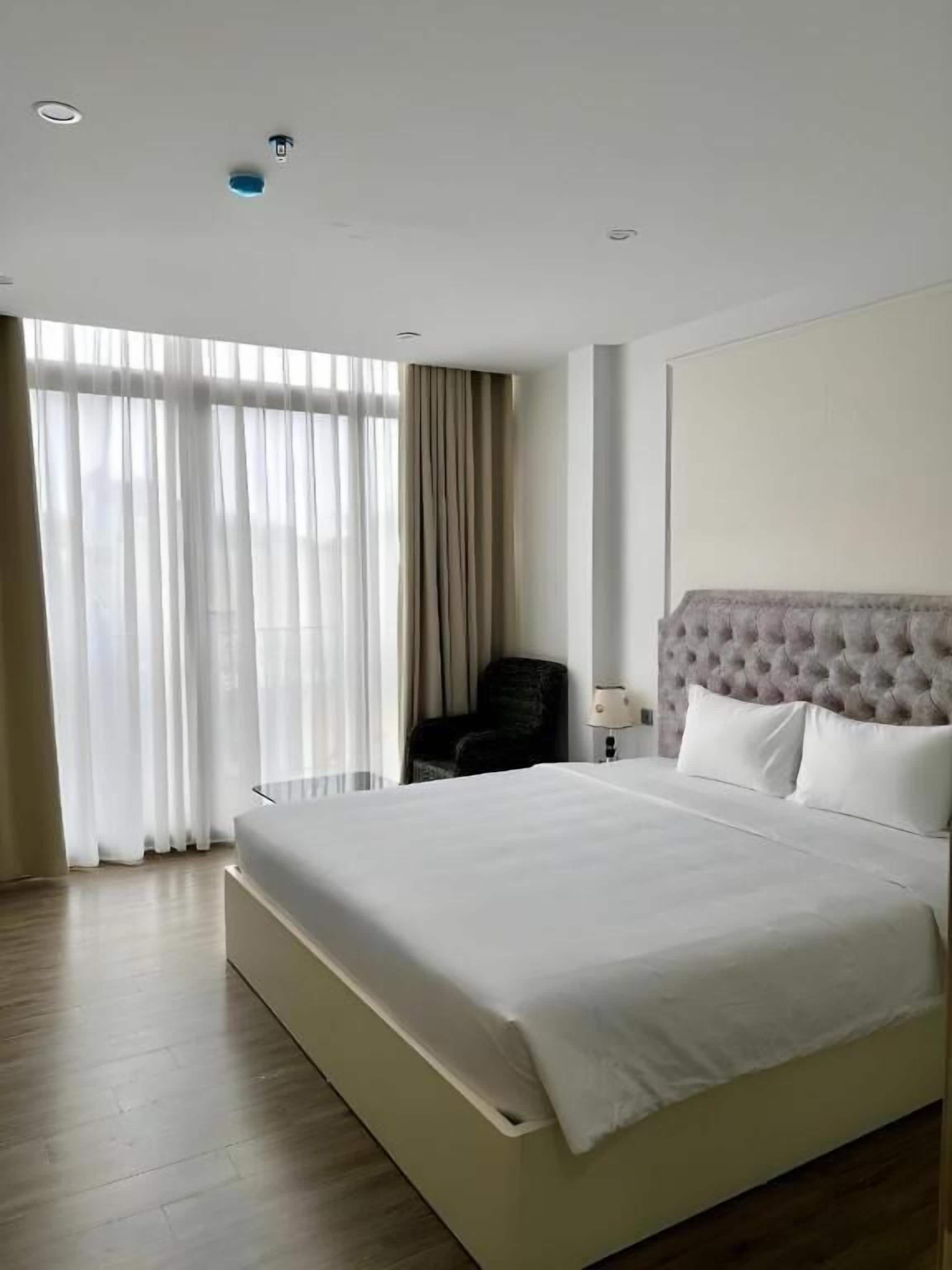 A hotel room with a large bed, a chair, a nightstand, and a window with curtains.