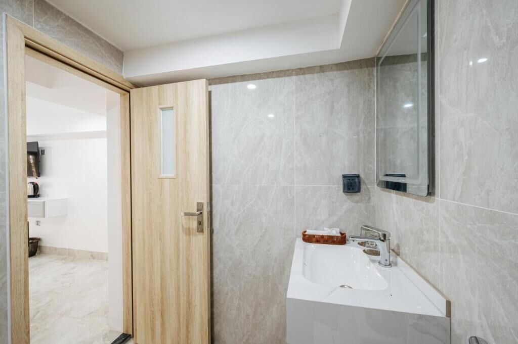 Un baño con puerta de madera, un lavamanos blanco, un espejo y un perchero para toallas.