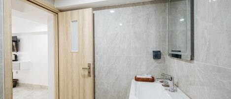 Un baño con puerta de madera, un lavamanos blanco, un espejo y un perchero para toallas.
