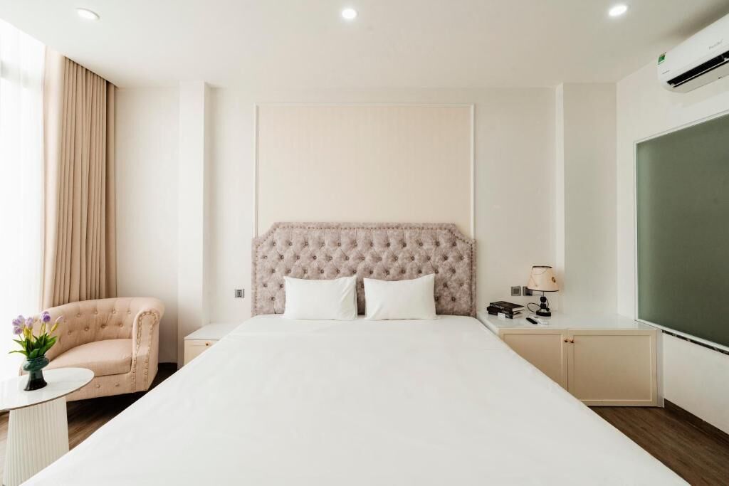 A hotel room with a large bed, a bedside table, a lamp, a chair, and a view of the outside.