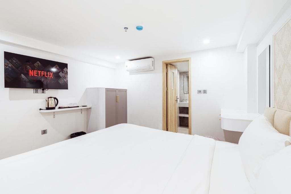 A modern hotel room with a large bed, a TV mounted on the wall, a wardrobe, and a bathroom visible through an open door.