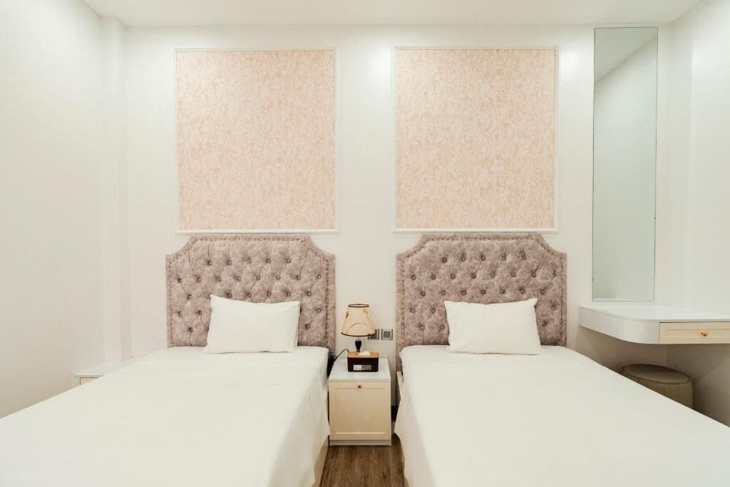 A hotel room with two beds, a nightstand with a lamp, a mirror, and a small table.