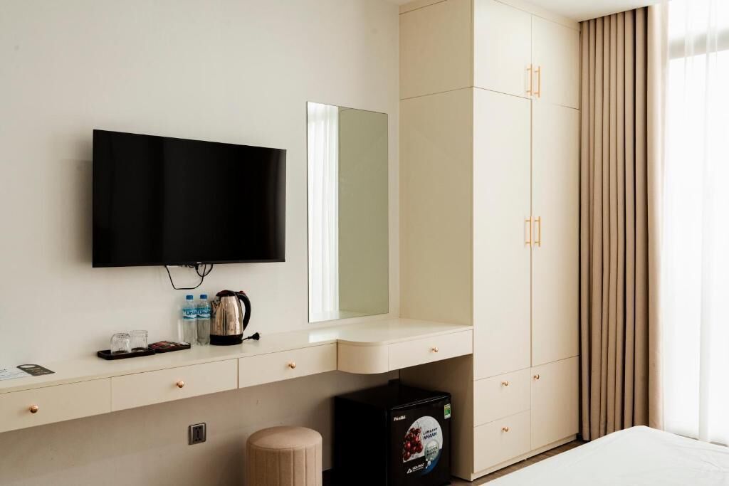 A hotel room with a flat-screen TV, a minibar, a large mirror, and a wardrobe.