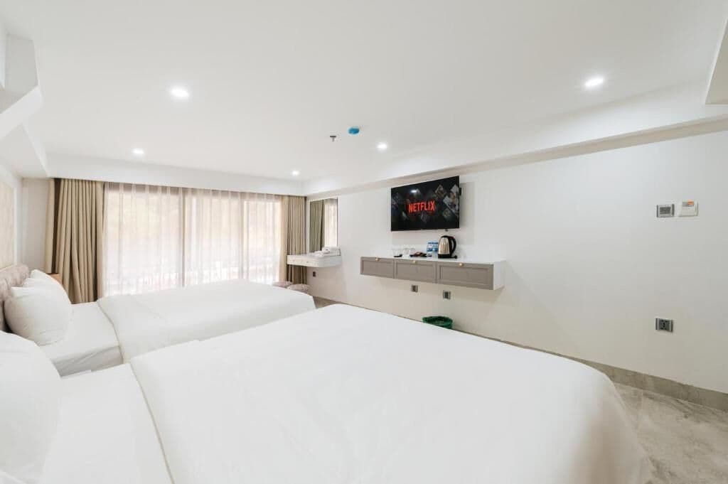 Una habitación de hotel con dos camas, un televisor montado en la pared, una cafetera y una ventana con cortinas.