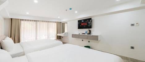 Una habitación de hotel con dos camas, un televisor montado en la pared, una cafetera y una ventana con cortinas.