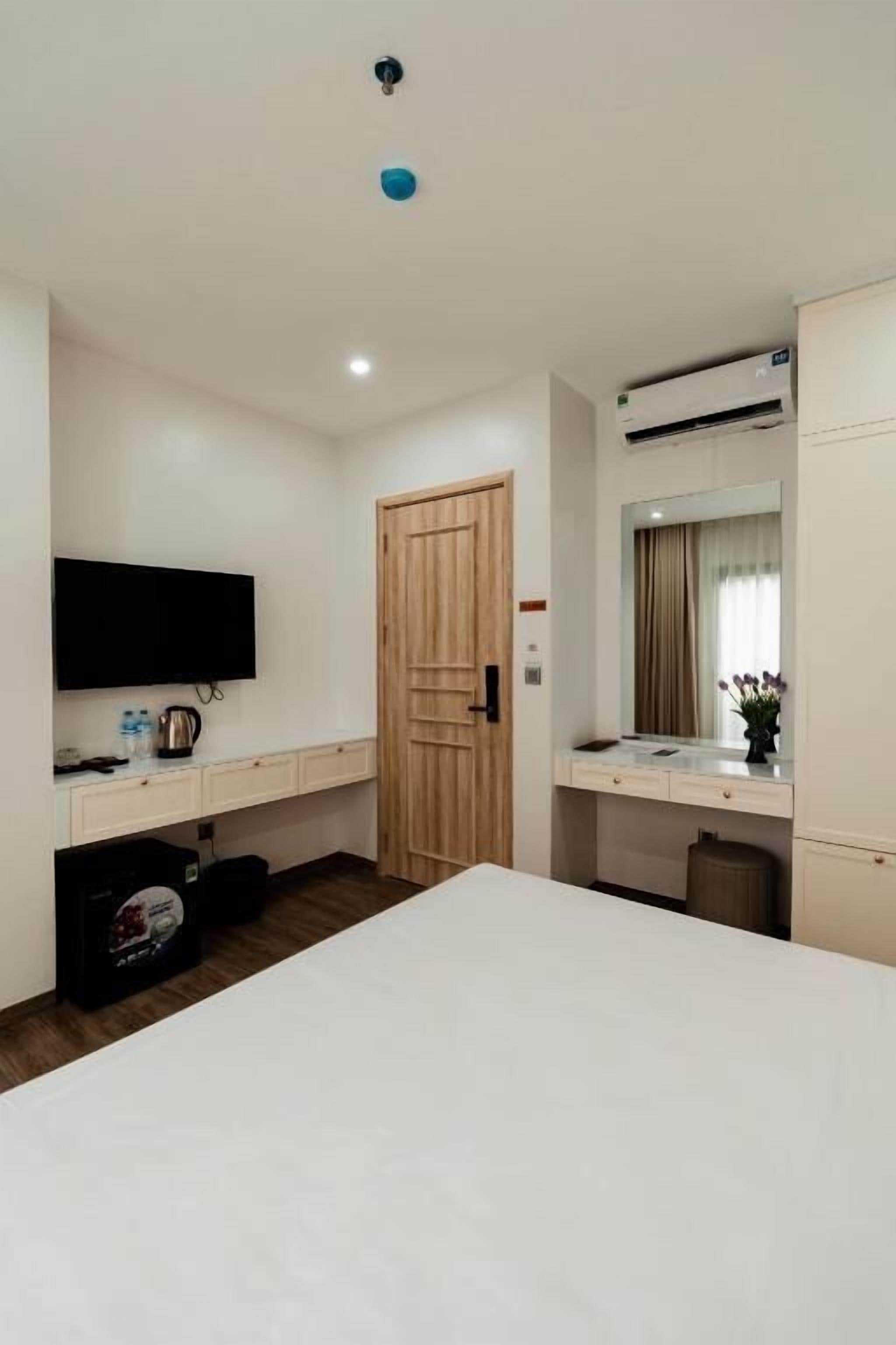 A hotel room with a bed, a TV, a wooden door, a mirror, and a small kitchenette.