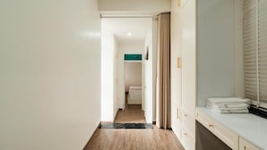 A hallway with a wooden floor, a bed in the distance, and a bathroom with a sink and towel stack. - Hanoi Serenity Hotel (Hanoi)