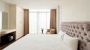 A hotel room with a large bed, a television on the left, a small table with a vase, and a chair. - Hanoi Serenity Hotel (Hanoi)