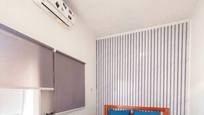 Ett hotellrum med en säng, ett fönster med persienner, en väggmonterad luftkonditioneringsanläggning och en randig vägg.