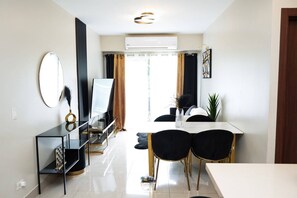 Un comedor moderno con una mesa de vidrio, sillas negras, una consola negra con un espejo y una planta en maceta.
