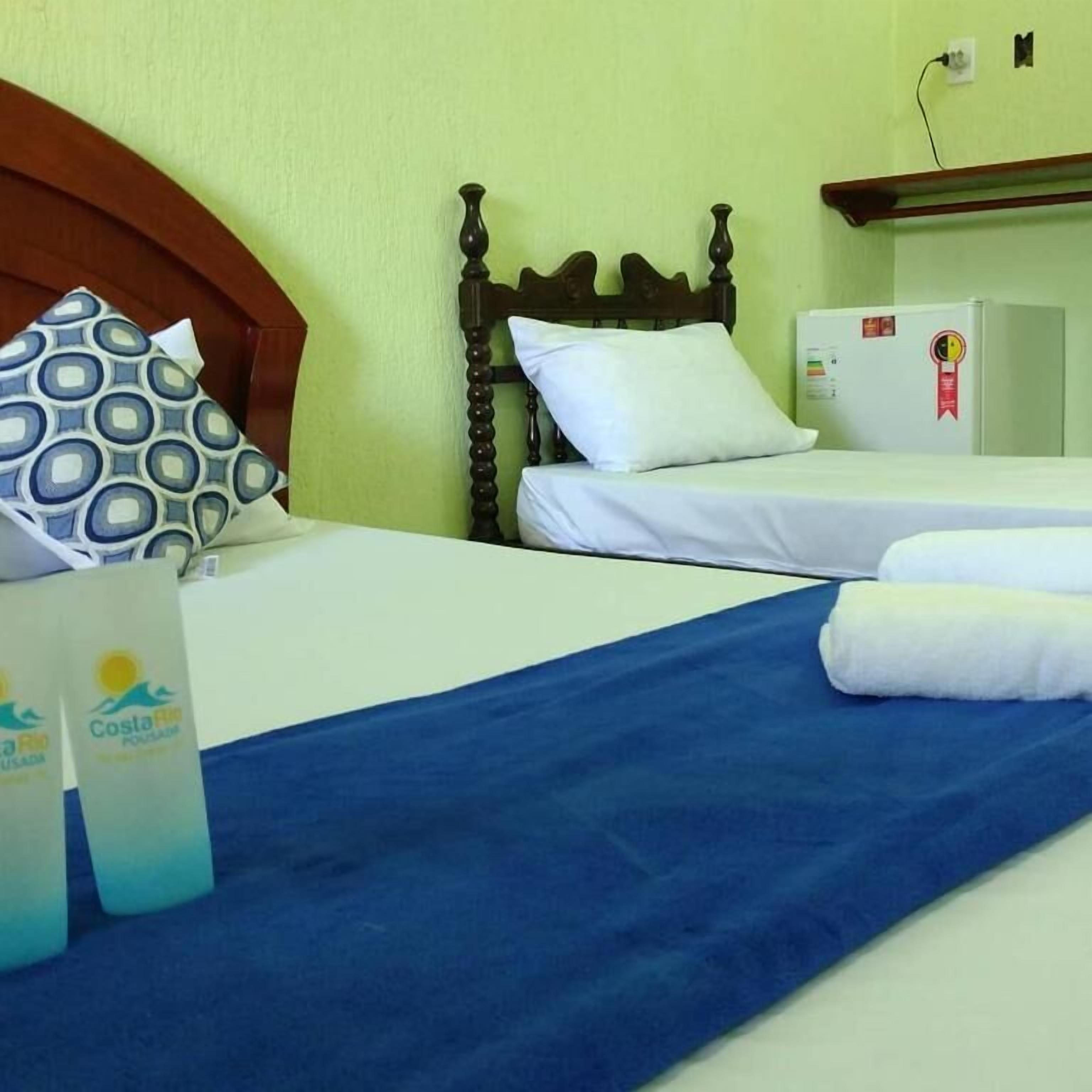 Quarto de hotel com uma cama, um pequeno frigorífico e uma toalha azul.