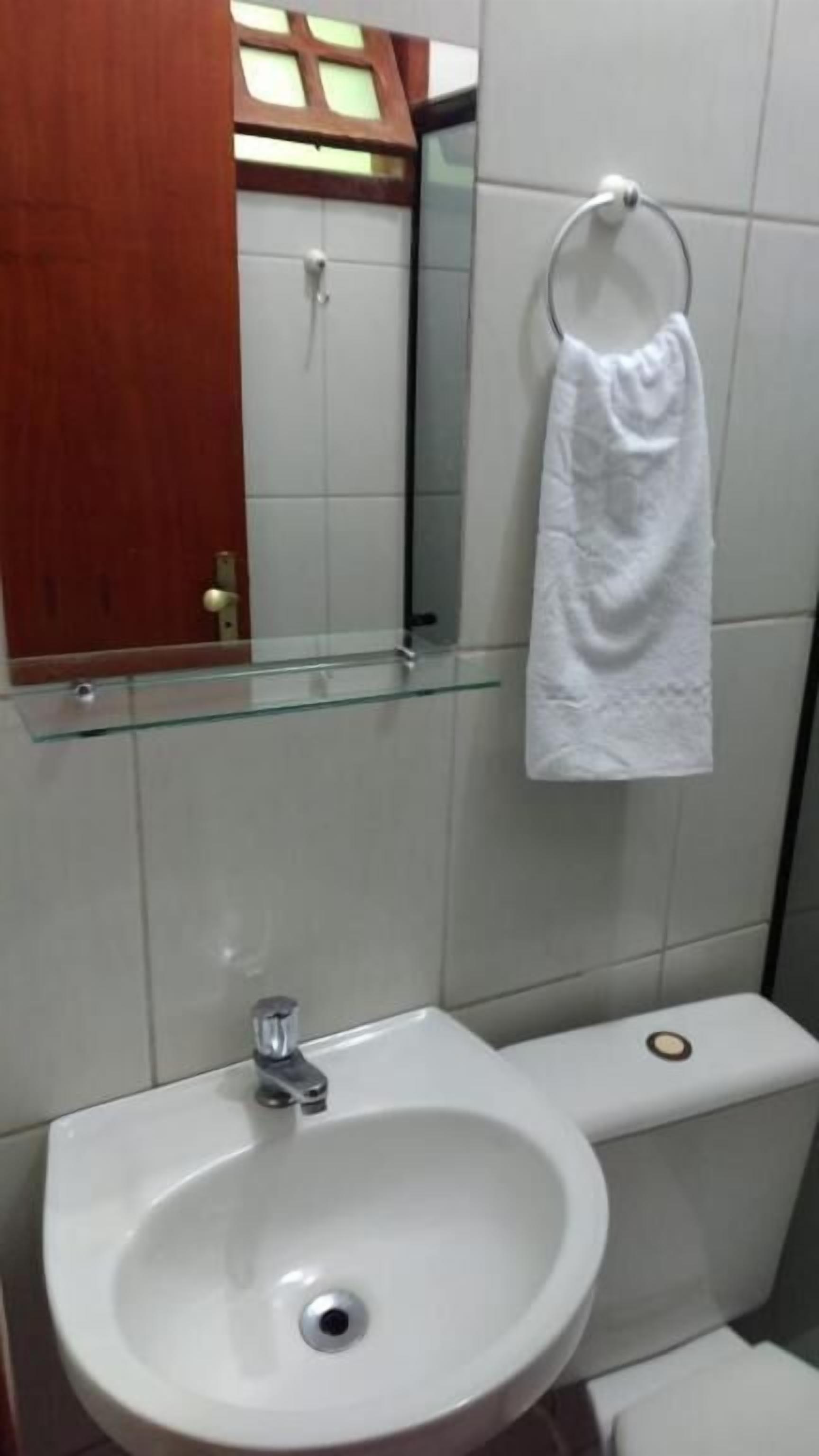 A bathroom with a glass shelf, a sink, a toilet, and a towel hanging on a metal ring.