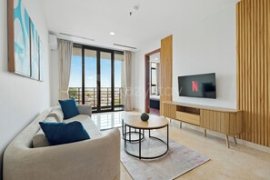 A modern living room with a sofa, a coffee table, a TV, and a balcony view. - Girava by Kozystay - Dago (Bandung)