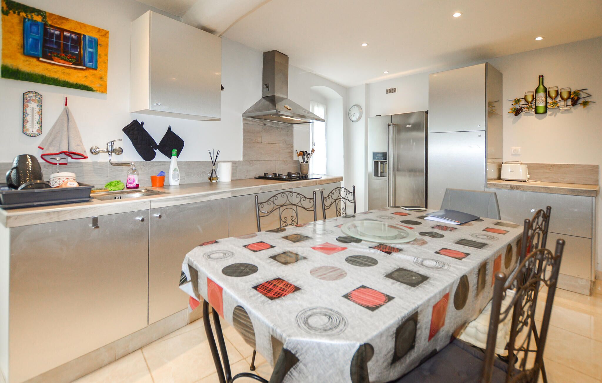 A modern kitchen with a central island, stainless steel appliances, and a dining area with a patterned tablecloth.