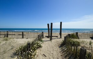 Ein sandiger Strand mit hölzernen Pfählen und einem Zaun, der zum Meer führt.
