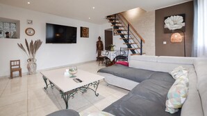Ein modernes Wohnzimmer mit Sofa, Esstisch, Treppe und Fernseher.