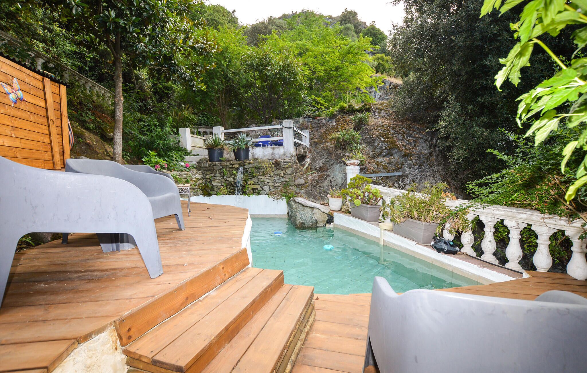 Eine Holzterrasse mit Pool, weißen Stühlen und einer Steinmauer mit Wasserfall.