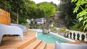 Eine Holzterrasse mit Pool, weißen Stühlen und einer Steinmauer mit Wasserfall.