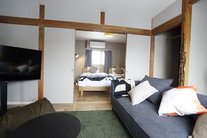 A modern hotel room with a bed, a sofa, a TV, and a wooden ceiling structure.