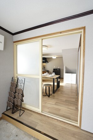 Una habitación con un espejo grande, suelo de madera, un área de comedor con mesa y sillas, y una cocina al fondo.