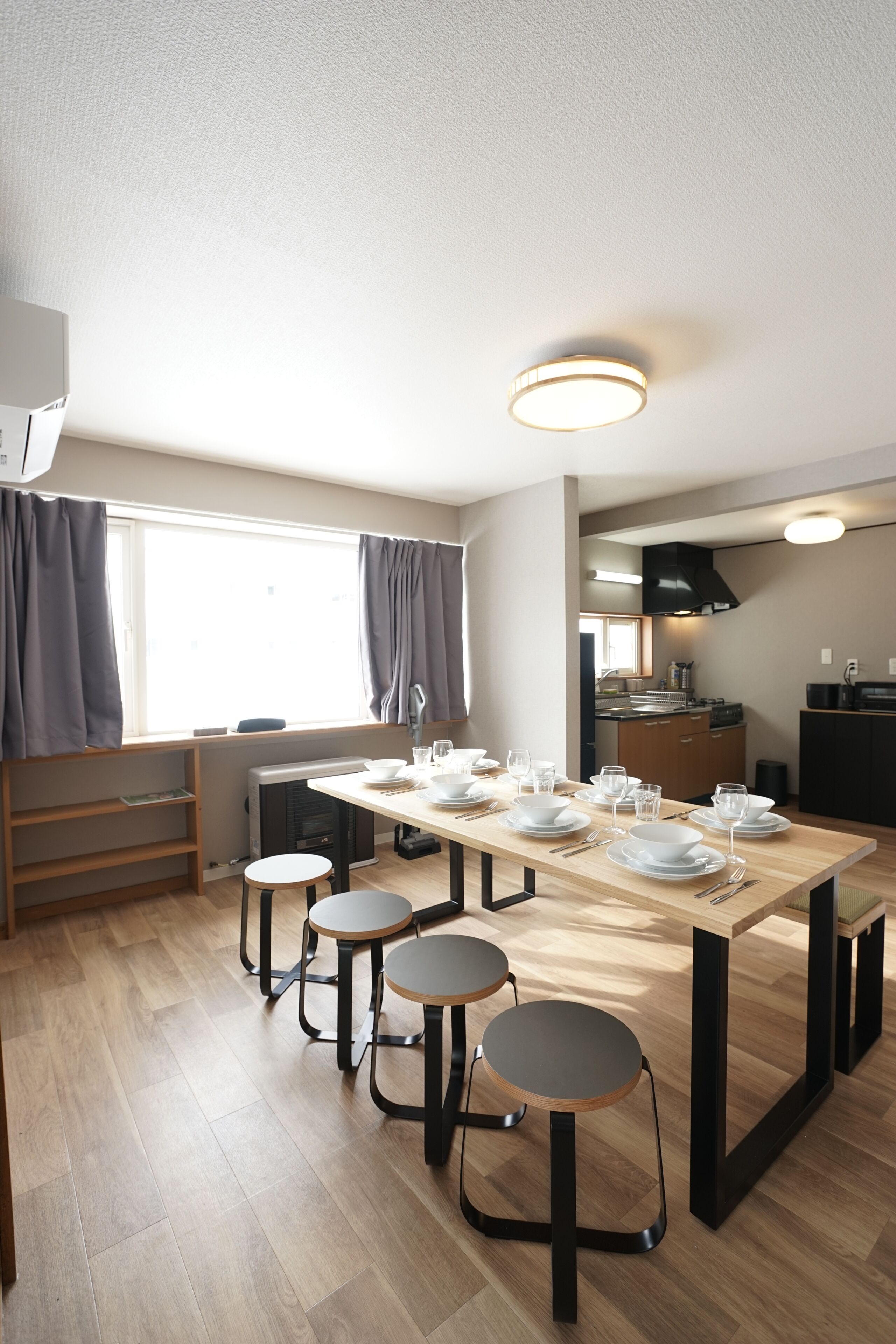 A modern kitchen with a dining table set for four, a built-in oven, and a window with curtains.