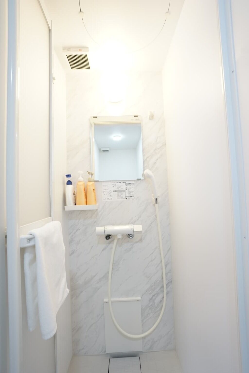 Un baño pequeño y moderno con ducha, un espejo y un estante con artículos de aseo.