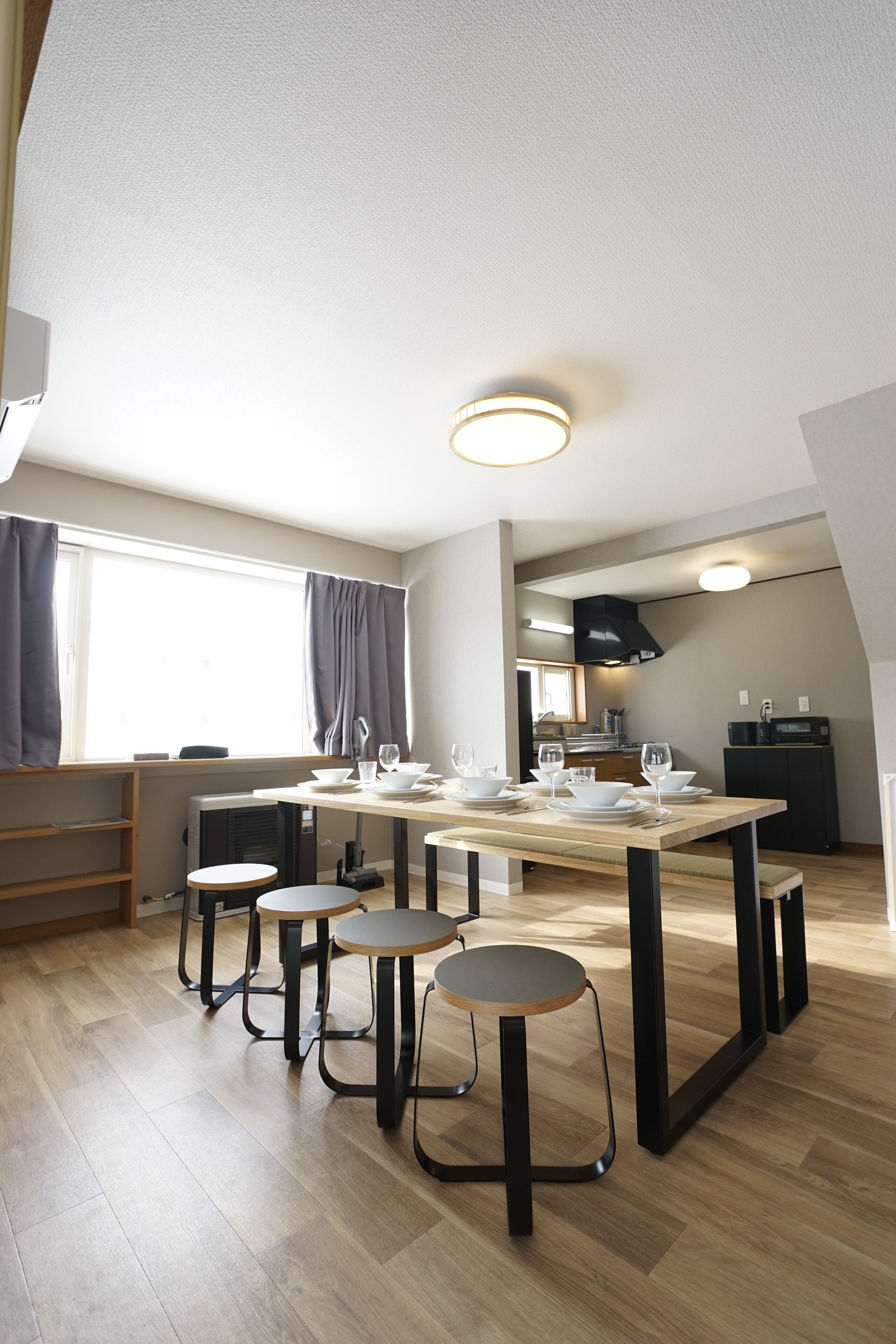A modern kitchen with a dining table set for four, a built-in oven, and a window with curtains.