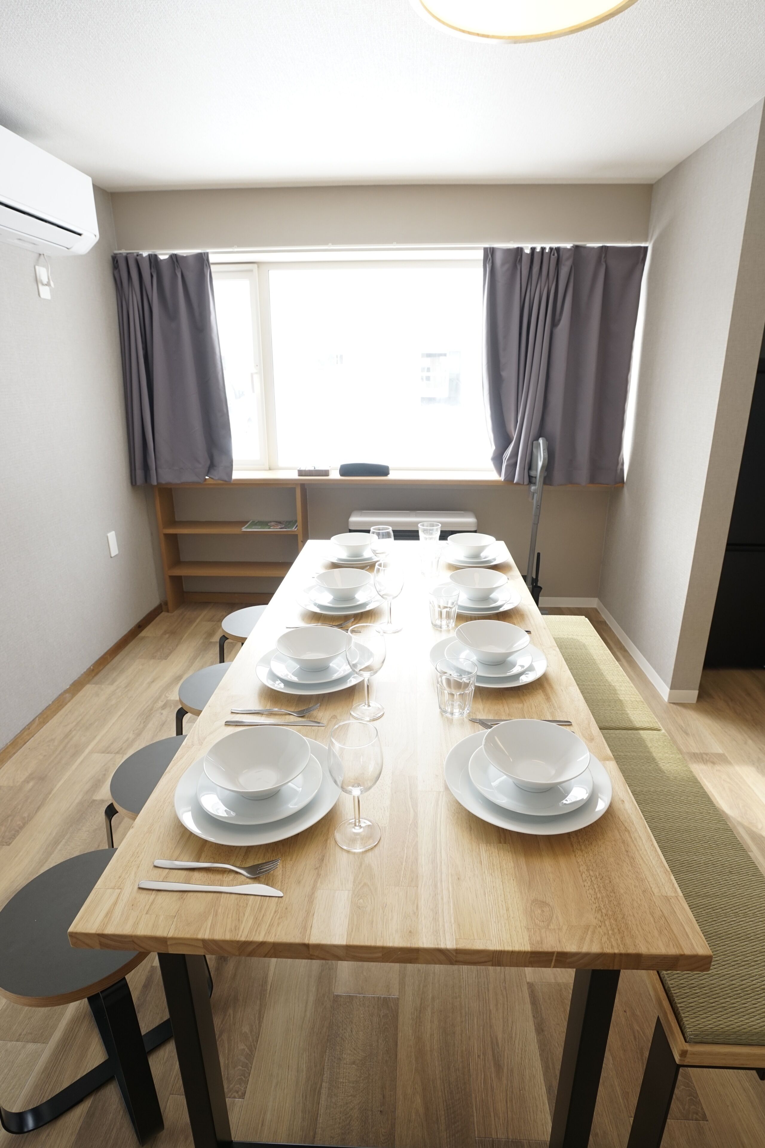 A dining area with a long wooden table set for six, chairs, and a window with curtains.