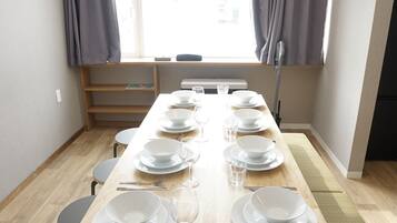 A dining area with a long wooden table set for six, chairs, and a window with curtains.